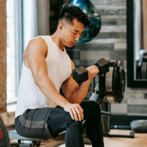 Fit Asian man exercising with dumbbell in gym