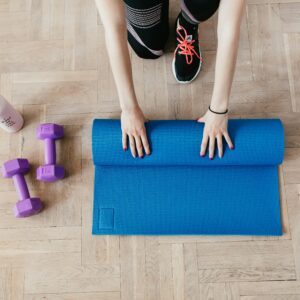 Crop sportswoman unfolding sport mat on wooden floor