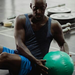 Man in Black Tank Top and Blue Shorts Using green Gym Ball